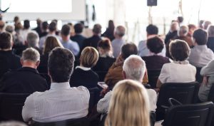 Audience of middle-aged professionals watching keynote consulting presentation.